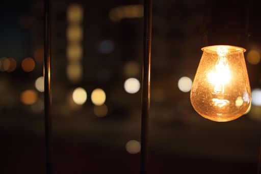 A closeup of an illuminated lightbulb and poles in the street on the background of bokeh lights