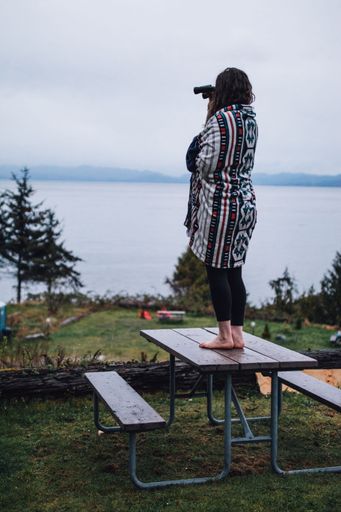 woman standing on picnic table with binoculars, looking out at ocean to Canada, Pacific Northwest