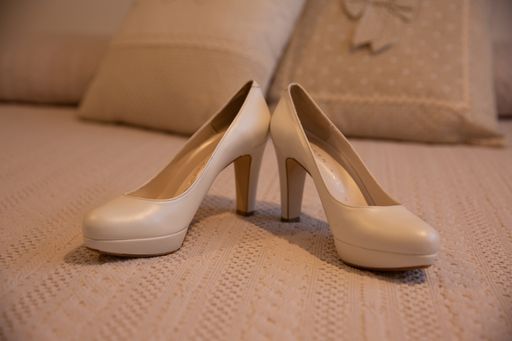 A closeup shot of a pair of beautiful wedding high heels on the woven sheets on a bed