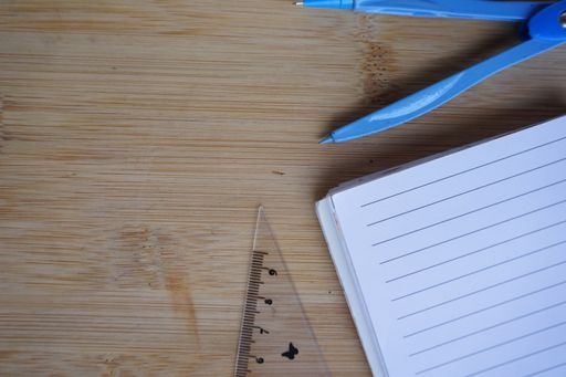 A top view of a compass with an open notebook and a ruler on a wooden surface