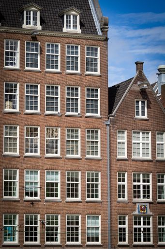 A vertical shot of the facade of a brick building with wooden white windows under the blue sky