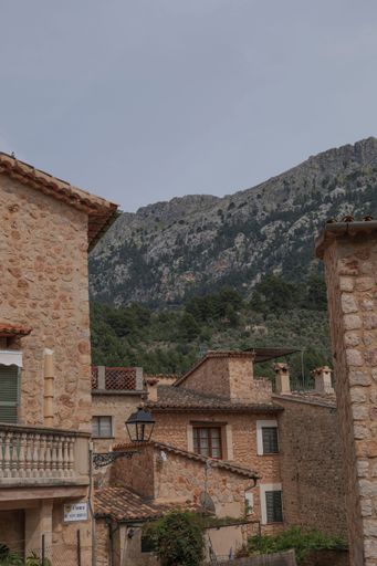 A vertical shot of old stone buildings in Fornalutx, Mallorca against green mountains