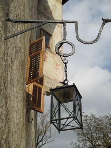A vertical shot of a street lamp hanging from a decorative hook on the wall at daytime