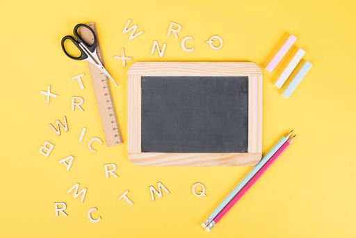 Empty chalkboard with colorful chalk, pencils, ruler, letters and a scissor, back to school and education concept