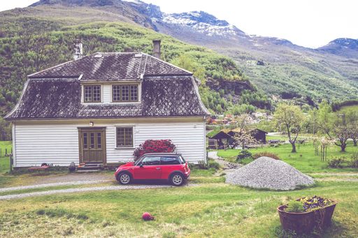 A beautiful shot of a wooden house with a parked red car in a village and surrounded by mountains