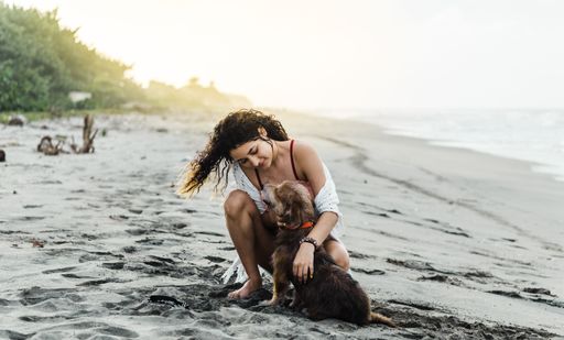 A closeup of a young Hispanic female hugging her brown dog on the beach