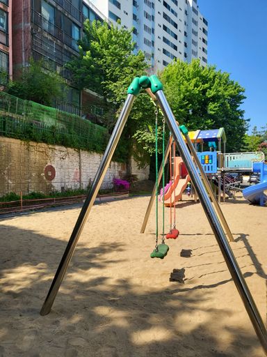 A vertical shot of empty swings with colorful seats in a playground with sand on the ground