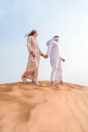 A White couple walking in a desert wearing abayas