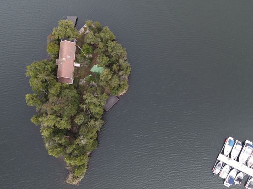 An aerial shot of a little private island in the middle of a lake with a  house
