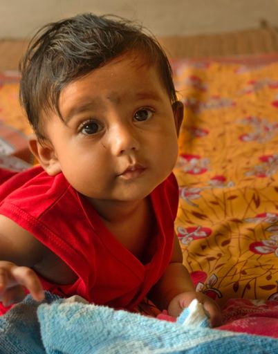 Aute Indian baby lying on bed sheet over a mat looking at the camera. Selective focus on baby's face.
