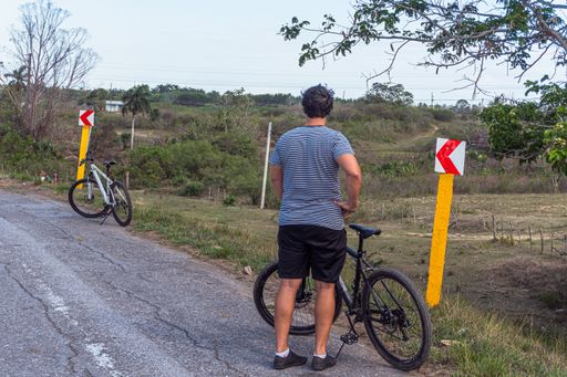 A man resting on the edge of the road with two bicycles parked next to him