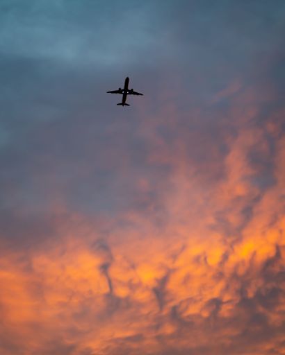 A vertical low angle shot of an airplane in a dramatic sky with colorful clouds