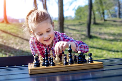 A selective focus shot of an adorable girl wearing a checkered shirt playing chess