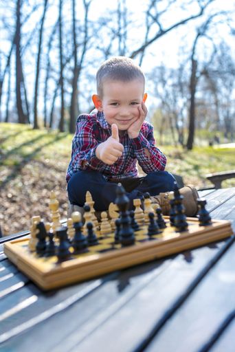 A selective focus shot of an adorable boy wearing a checkered shirt playing chess