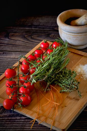 A top view of the fresh cherry tomatoes and green herbs on a wooden board