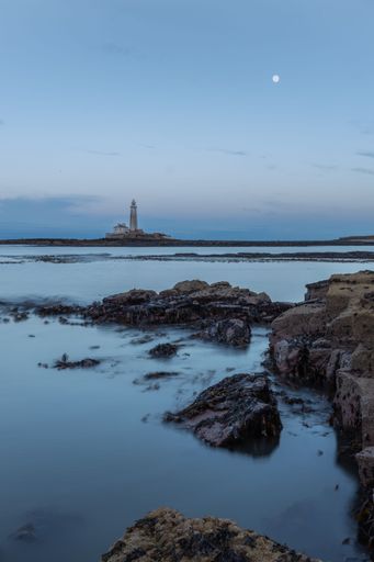 A vertical shot of St Mary's lighthouse surrounded by rocks and water