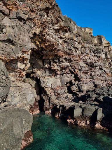 A vertical shot of rocky island and calm coast under a clear sky