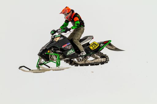 Snowmobiler jumping high above the track. On a snowmobile, a sportsman. It's a overcast day for a winter competition.