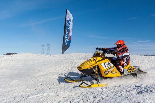 Snowmobile competing in extreme sports. Snowmobile jumps high above the track. On a snowmobile, a sportsman. It's a sunny day for a winter competition