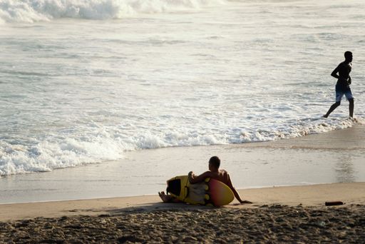 A bright summer day with a surfer sitting on the shore of Farol da Barra beach in Salvador, Brazil