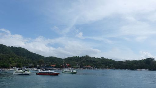 A summer day outdoors at an island with boats floating on the clear waters surrounded by lush greenery