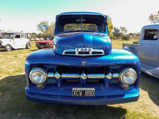 Old blue Ford F 1 V8 1950s utility pickup truck in the countryside. Front view. Grill. Nature grass and trees. Classic car show.