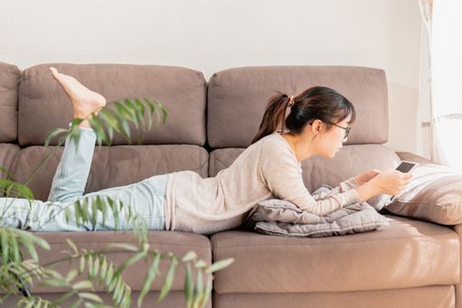 A young Asian woman lying on the couch and watching videos on a tablet