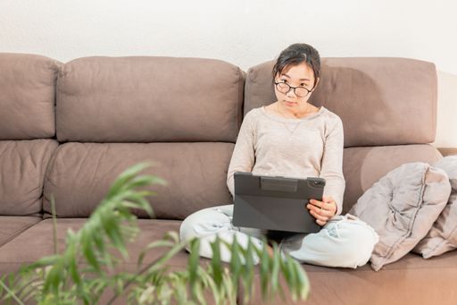 A young Asian woman working on a tablet from home because of COVID-19 quarantine