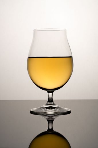 A vertical shot of a clear glass with yellow liquid