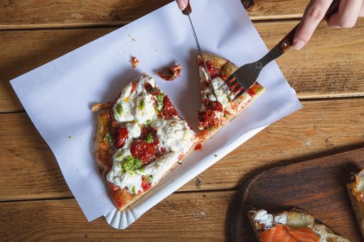A high angle shot of a person cutting a piece of pizza on a wooden surface