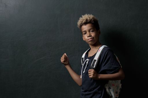 A black boy with a backpack posing on a dark grey background with copy space