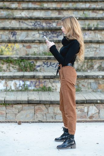 A young blond woman in a black turtleneck and beige trousers typing on her phone