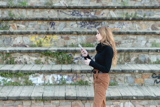 A young blond woman in a black turtleneck and beige trousers typing on her phone