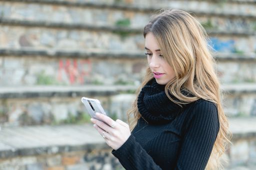 A young blond woman in a black turtleneck typing on her phone