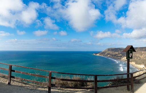 A landscape of the sea surrounded by hills under a blue cloudy sky and sunlight