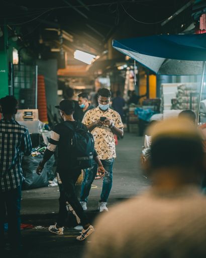 A person standing still with his phone as the world around him passes by in Little India, Singapore