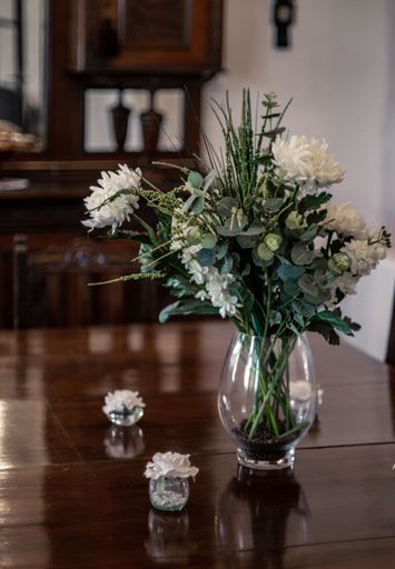 A vertical shot of a vase with white flowers on a wooden table in the living-room