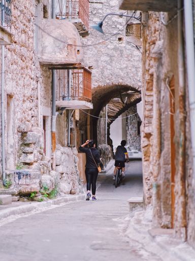 A vertical shot of a kid riding a bike past a woman walking at Pirgi, Chios, Greece