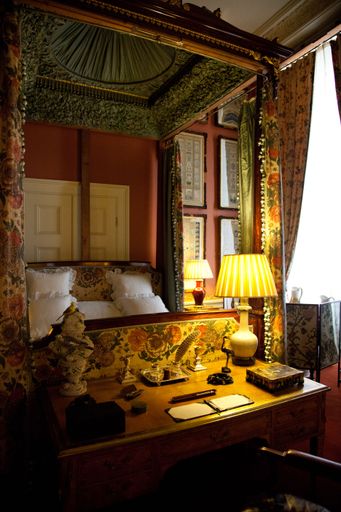 A vertical shot of furnished bedroom with ornate carved four-poster bed and matching antique desk with lamps