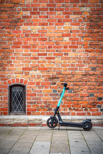 A vertical shot of a scooter parked on the sidewalk against a red brick wall