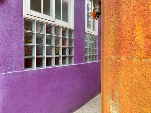 A narrow alley in between two buildings with purple and orange walls