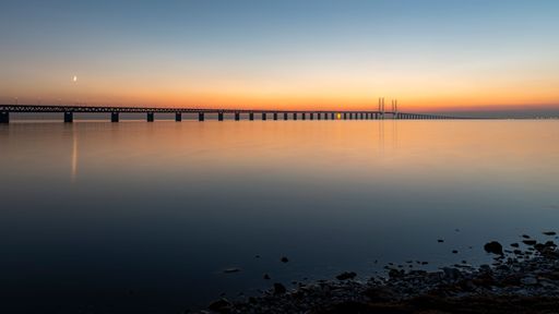 A scenic view of the Oresunds bridge captured from a rocky shore during a breathtaking sunset