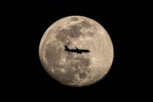 A scenic view of the silhouette of an airplane on the background of a beautiful big full moon