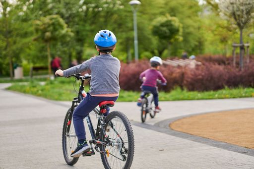 A vertical shot of two young boys with helmets riding a bicycle on the footpath in the Rataje park in Poznan, Poland