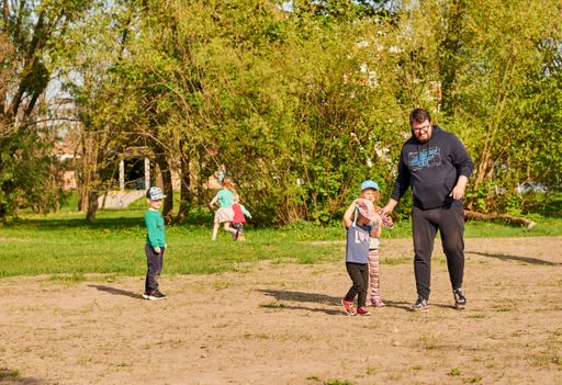 A man playing with children on ground close by trees in the Rataje park on a sunny spring day