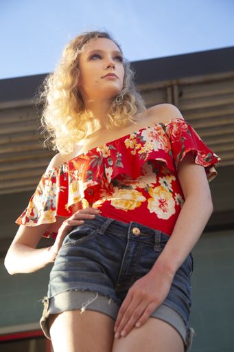 A beautiful blonde female with curly hair wearing a red off shoulder blouse and shorts