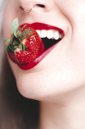 A vertical closeup shot of a young female with red lipstick biting strawberry - great for an article about cosmetics