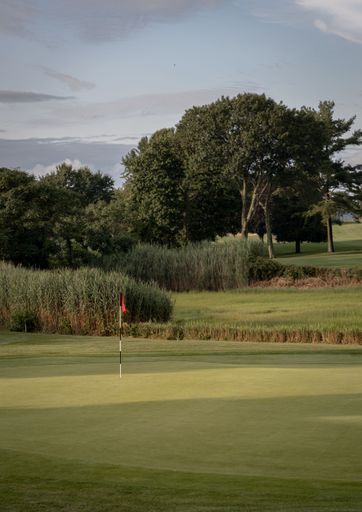 A vertical shot of a Golf course in Rhode Island between green grass and a blue cloudy sky