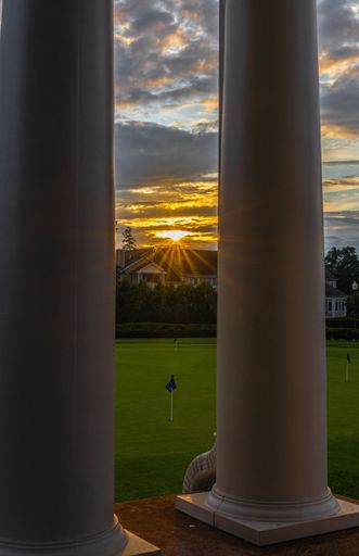 A vertical shot of a big columes next to a golf course and the sunset in the horizon