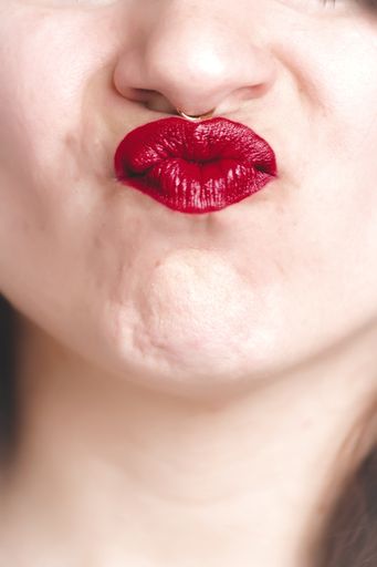 A vertical closeup shot of a female with a red lipstick making a duck face